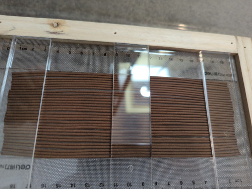 {My latest batch of sticks, partially dried and slightly wiggly, on a drying screen between two plastic rulers with three broad acrylic sticks on top of them.}